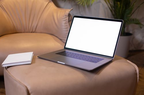 Free A sleek laptop on a leather sofa with a book, ideal for modern workspaces. Stock Photo