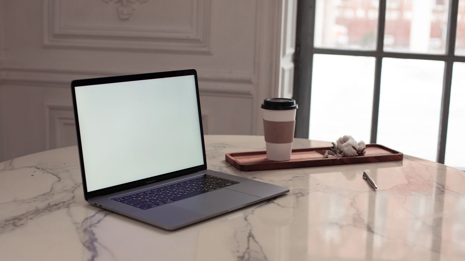 A laptop and takeaway cup on a marble table by a window
