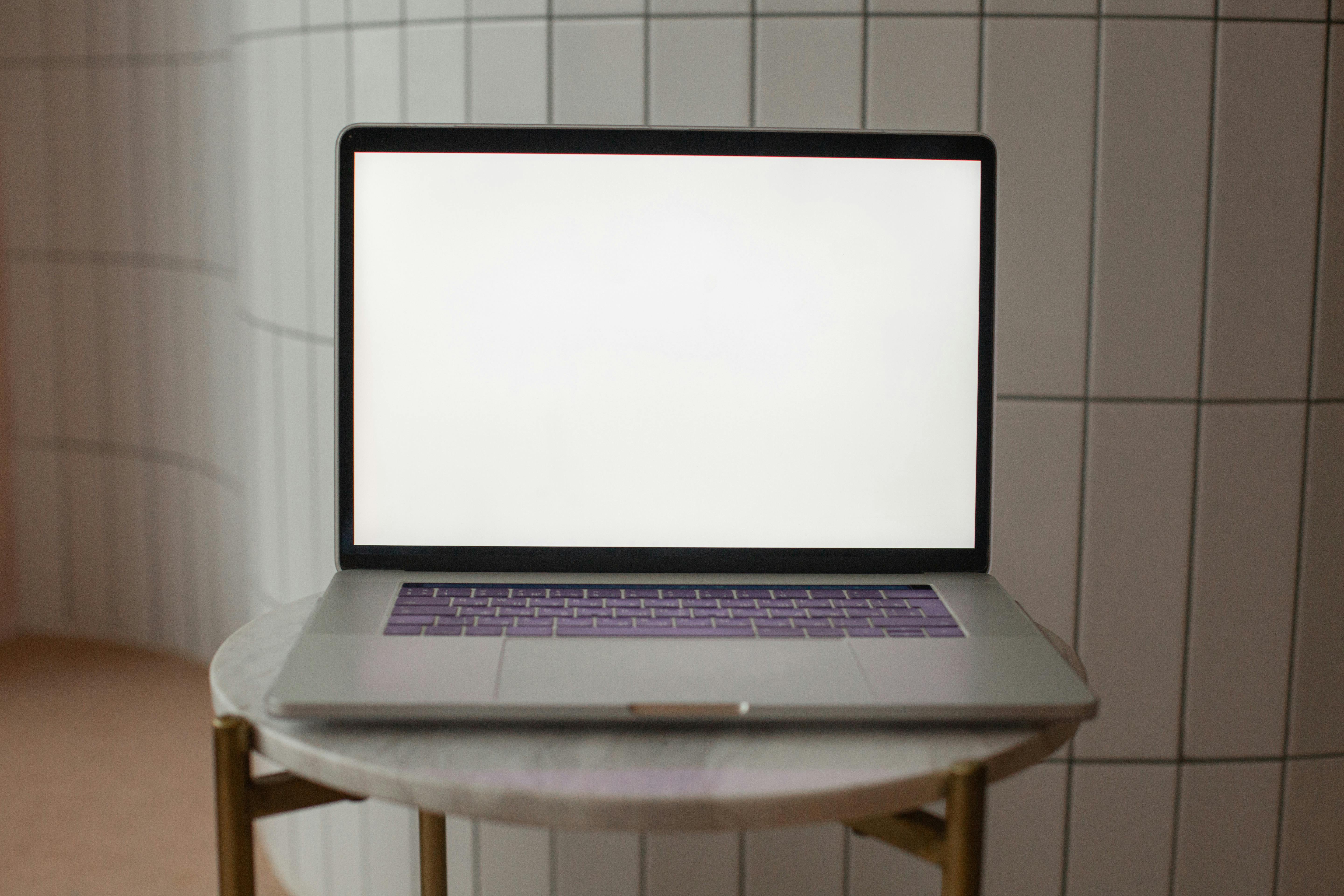 A laptop with a blank screen is positioned on a small round table, ideal for mockup use.