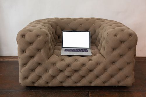 Free A laptop with a blank screen sits centered on a plush brown sofa, perfect for mockups. Stock Photo