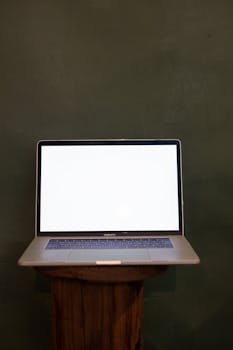 A modern laptop with a blank screen on a wooden stand against a dark green background.