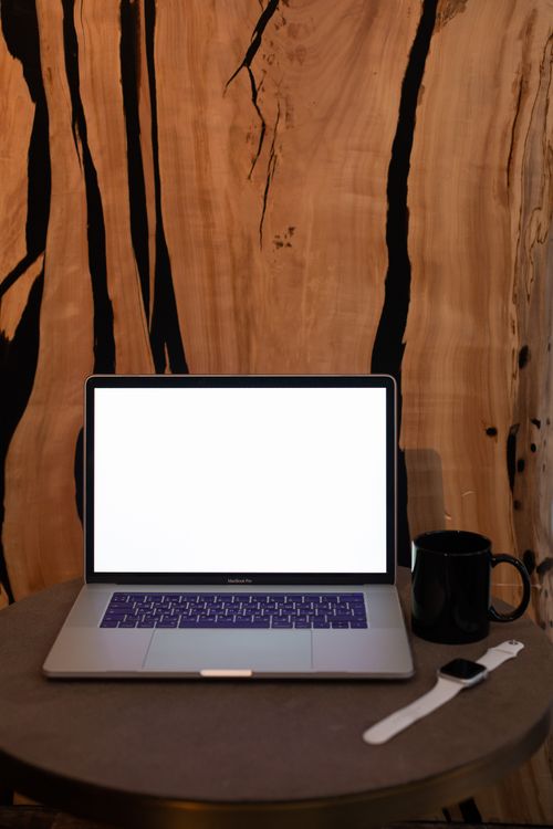 Free A clean and modern workspace featuring a laptop, coffee mug, and smartwatch on a table. Stock Photo