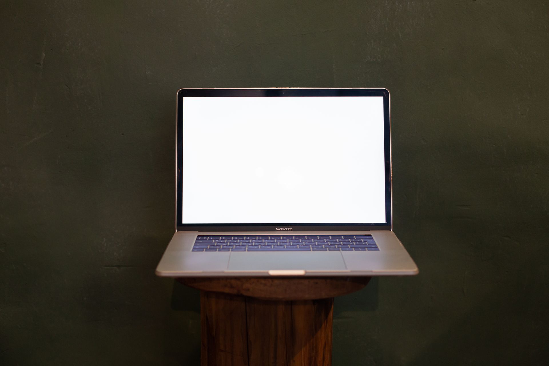 A sleek, modern laptop with a blank screen on a wooden stand against a green background.