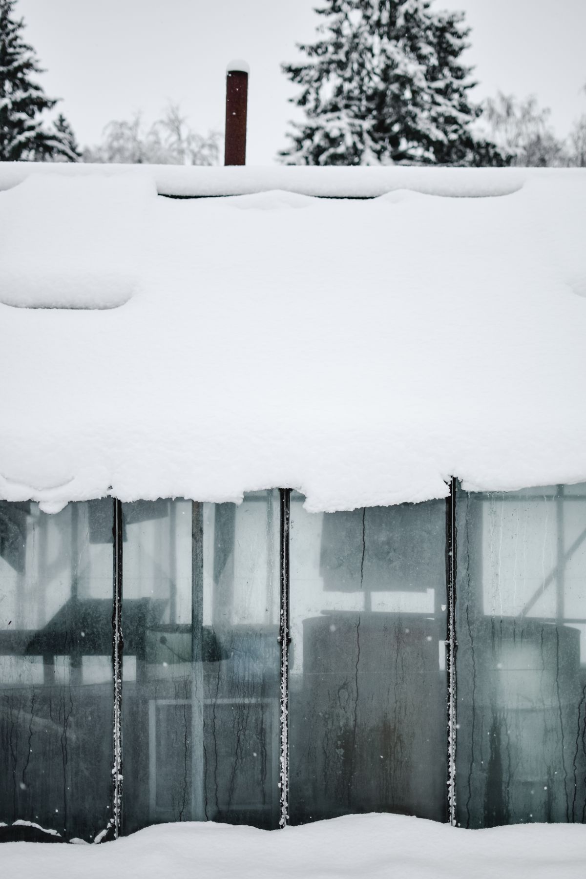 Schneebedecktes Glasdach eines Glasanbaus mit sichtbarem Rahmen, kalte Winterstimmung