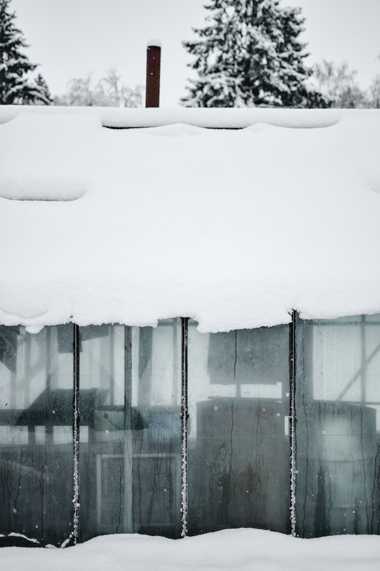 Snow Covered Roof Over A Glass Window