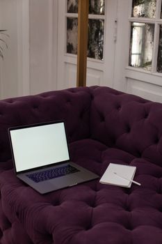 Laptop with blank screen on a purple couch, accompanied by a notebook and pen.