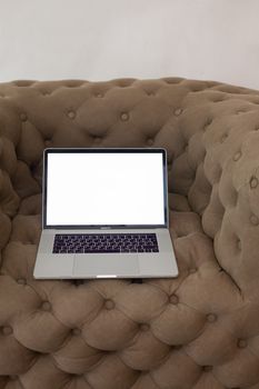 A laptop with a blank screen sitting on a plush tufted sofa indoors, perfect for design mockups.
