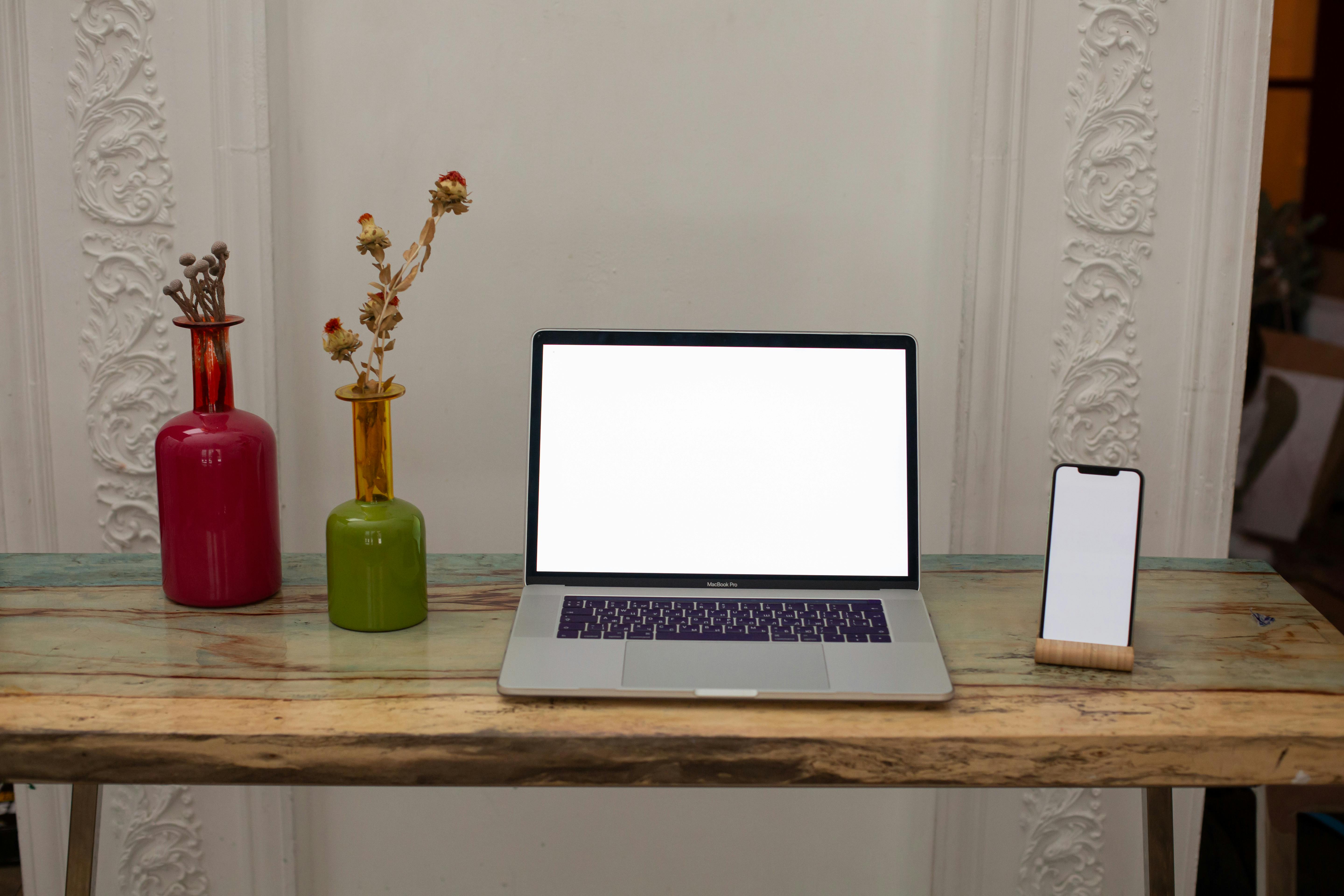 Minimalist desk setup featuring a blank laptop and smartphone with vibrant vases for a modern workspace aesthetic.