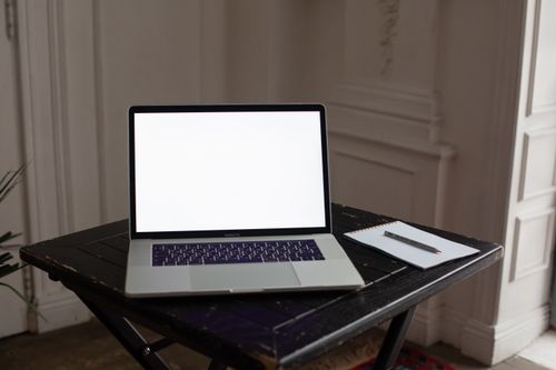 Free A minimalist home office setup featuring a laptop with a blank screen on a dark wooden table. Stock Photo