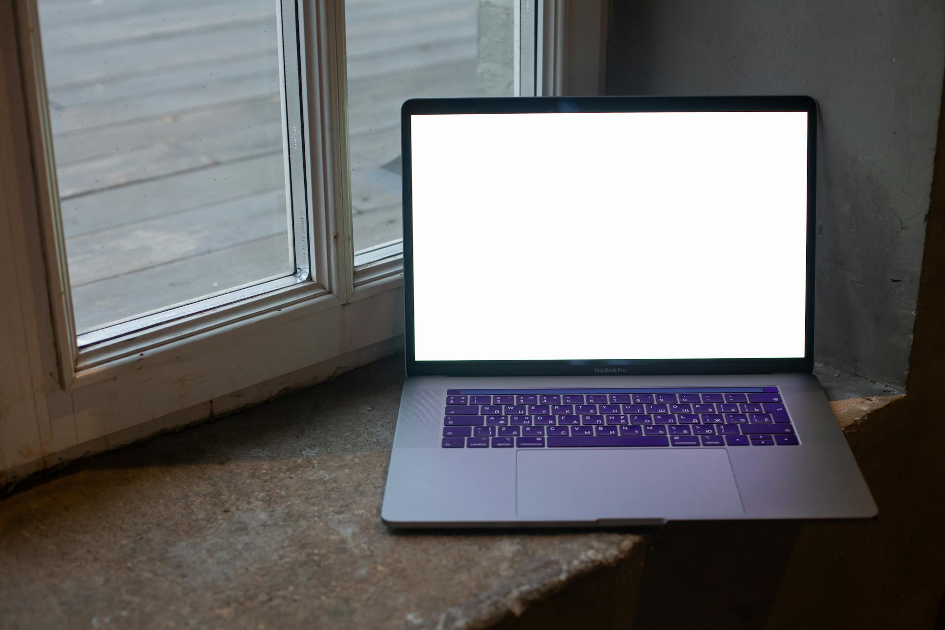 Open laptop with blank screen placed on stone windowsill, perfect for mockup use.