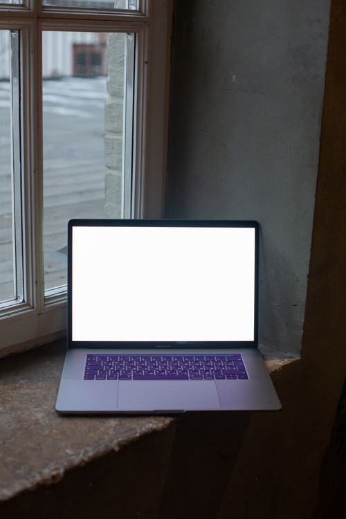 Free A laptop with a white screen placed on a window sill indoors. Stock Photo