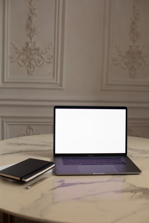 Free A sleek laptop with a blank screen sits on an ornate marble table in a classic interior setting. Stock Photo