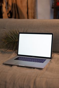 A sleek laptop with a blank screen resting on a comfortable sofa, ideal for mockup designs.