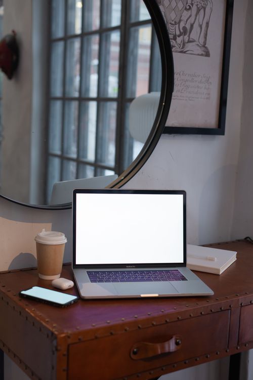 Free A stylish workspace featuring a laptop, coffee cup, and smartphone on a wooden desk. Stock Photo