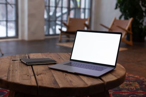 Free An open laptop on a rustic wooden table with a notebook, in a cozy indoor setting with natural light. Stock Photo