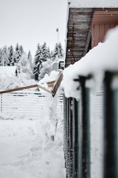 A winter scene showing snow being pushed off a fence with trees and buildings in the background.