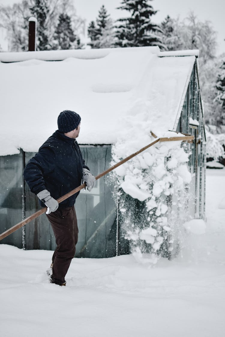 A Man Removing Snow On A Roof