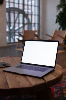 A blank laptop screen on a wooden table in a cozy, stylish room with natural light.