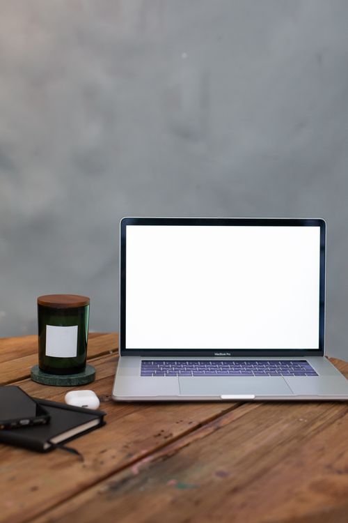 Free Minimalist workspace featuring a laptop, notebook, candle, and earphones on a wooden table. Stock Photo