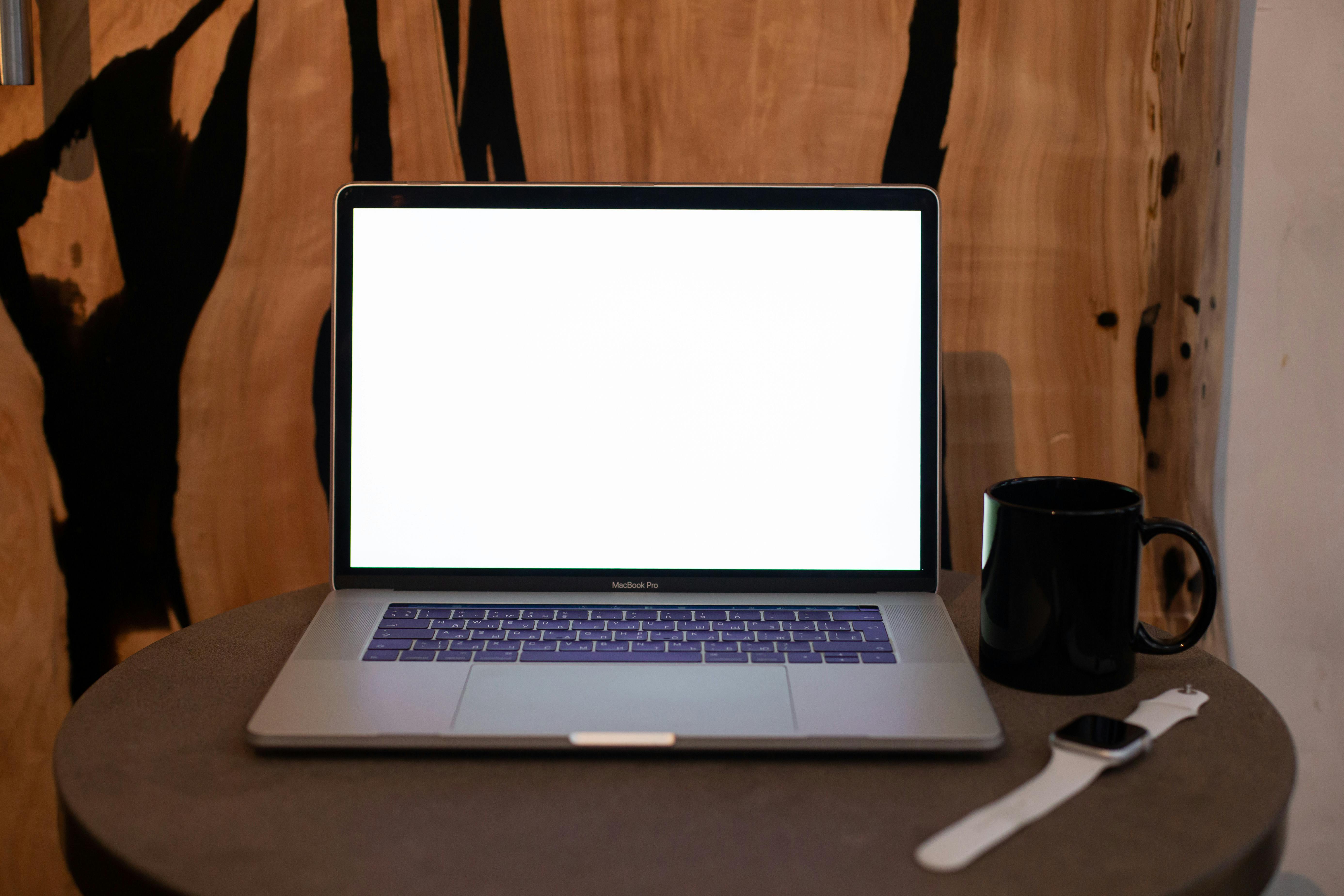A contemporary workspace featuring a laptop with blank screen, coffee mug, and smartwatch on a table.