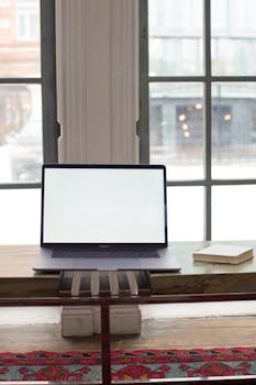A minimalist workspace featuring a laptop with a blank screen and a notebook on a wooden desk.