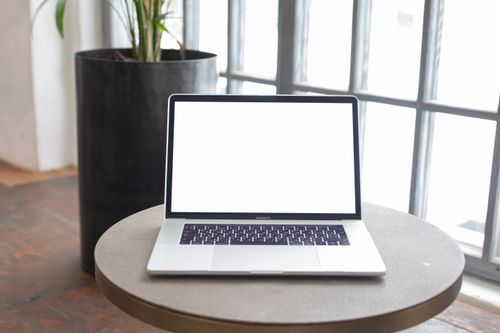 Free A sleek modern laptop with a blank screen sits on a round table in a bright office setting. Stock Photo
