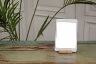 A modern tablet with a blank screen on a wooden table, featuring indoor plants.
