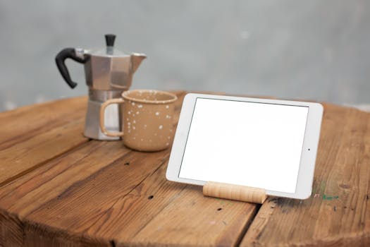 Mockup of a tablet next to coffee pot and mug on rustic table.