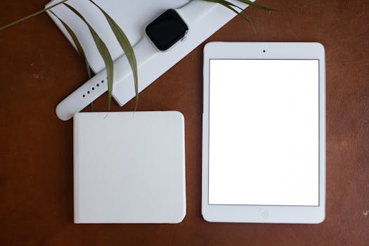 Flat lay of a smartwatch, tablet, and notebook on a brown table, ideal for technology and lifestyle themes.