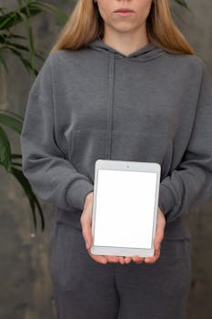A woman in a grey hoodie holds a blank tablet, perfect for mockups.