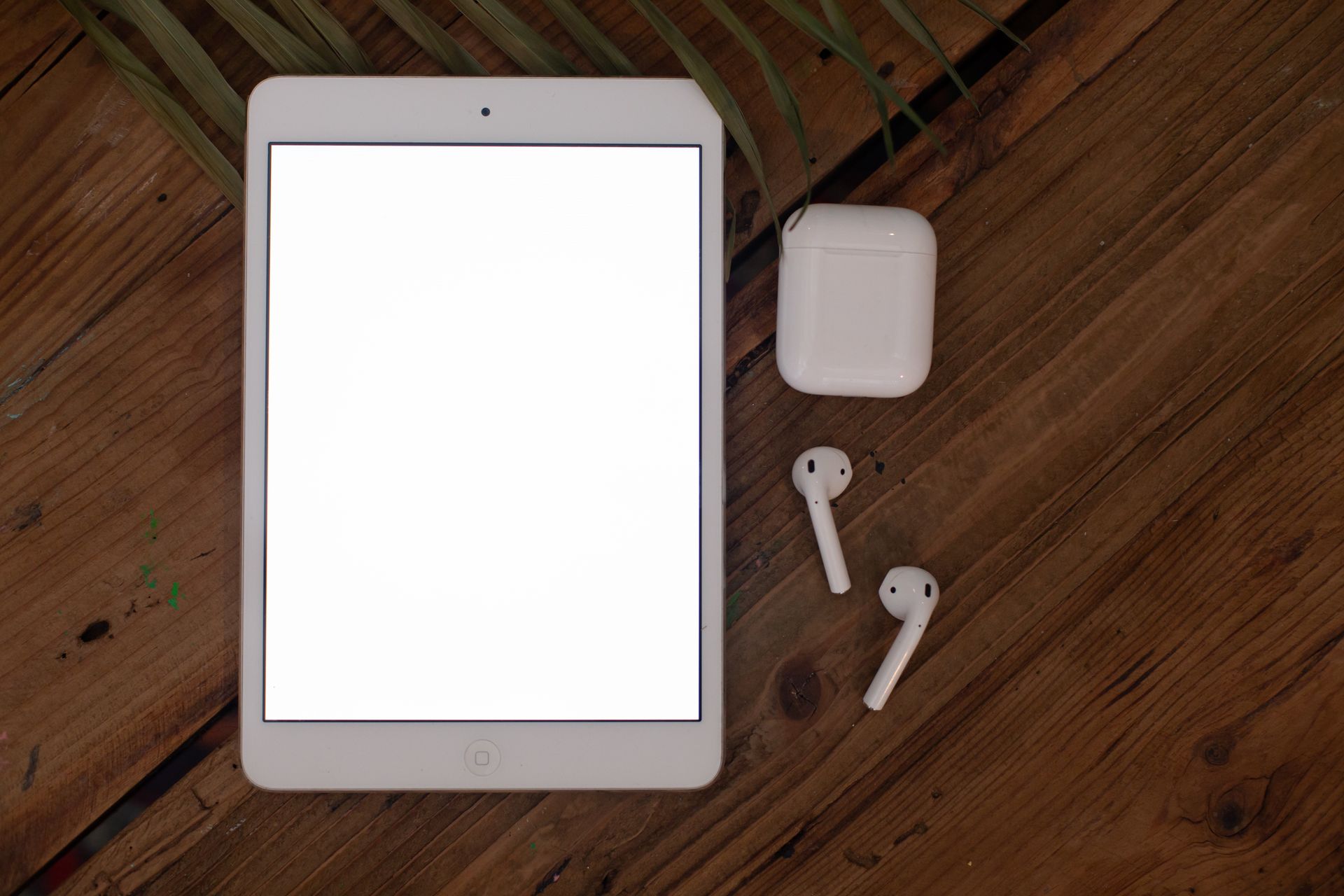 Flatlay of a tablet and wireless earbuds on a wooden surface, perfect for tech mockups.