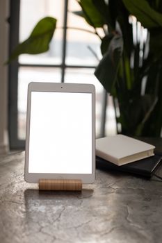 Vertical shot of a blank tablet on a stand, next to books in a cozy indoor setting.