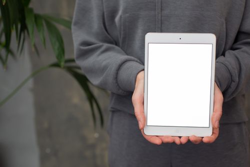 Free A person in grey clothing holding a tablet with a blank screen, ideal for mockup designs. Stock Photo
