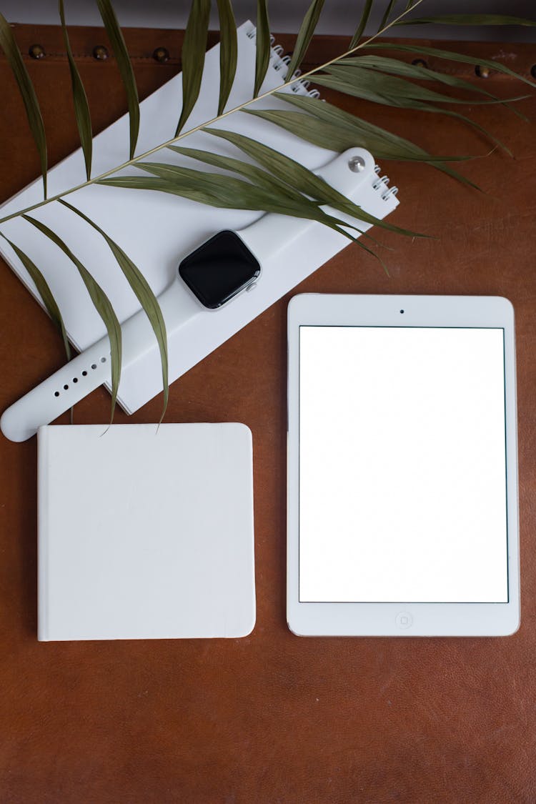 A Smartwatch On A Notepad Beside A Tablet With Blank Screen