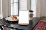 A Tablet with Blank Screen on a Wooden Table with a Delicious Croissant and Coffee