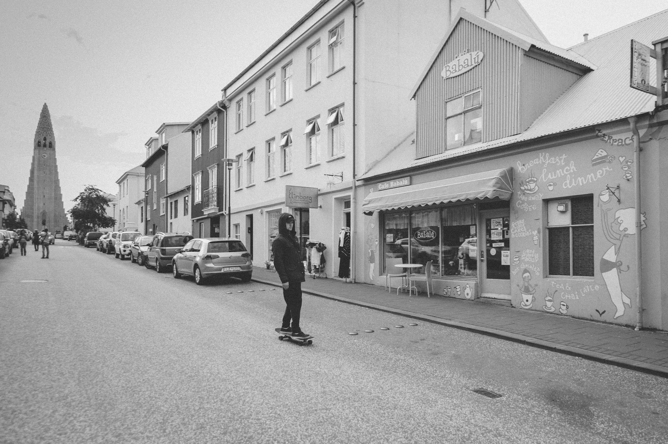 A skateboarder rides down a lively street in Reykjavik, Iceland with Hallgrímskirkja in the background.