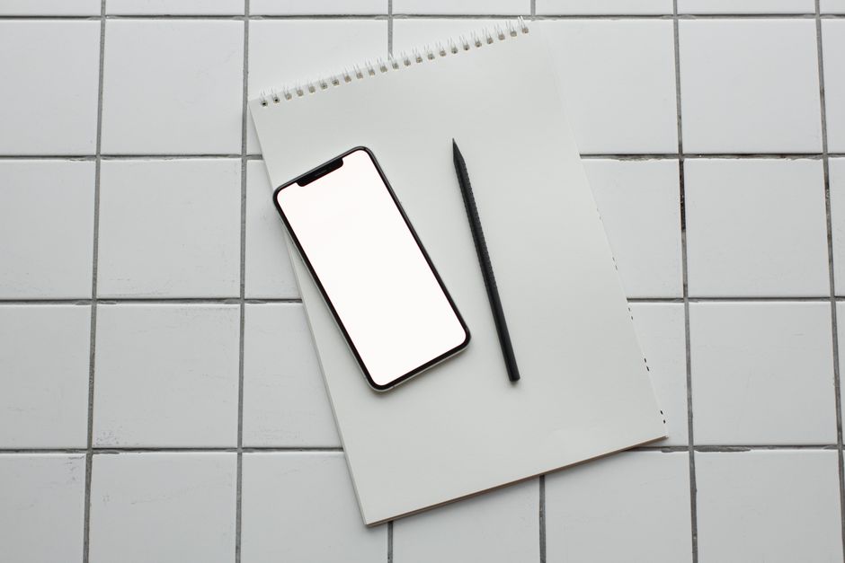 Flatlay of a smartphone and notebook on a tiled surface, ideal for tech and productivity themes.