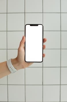 Hand holding a smartphone with blank screen in front of a tiled background, ideal for mockups.