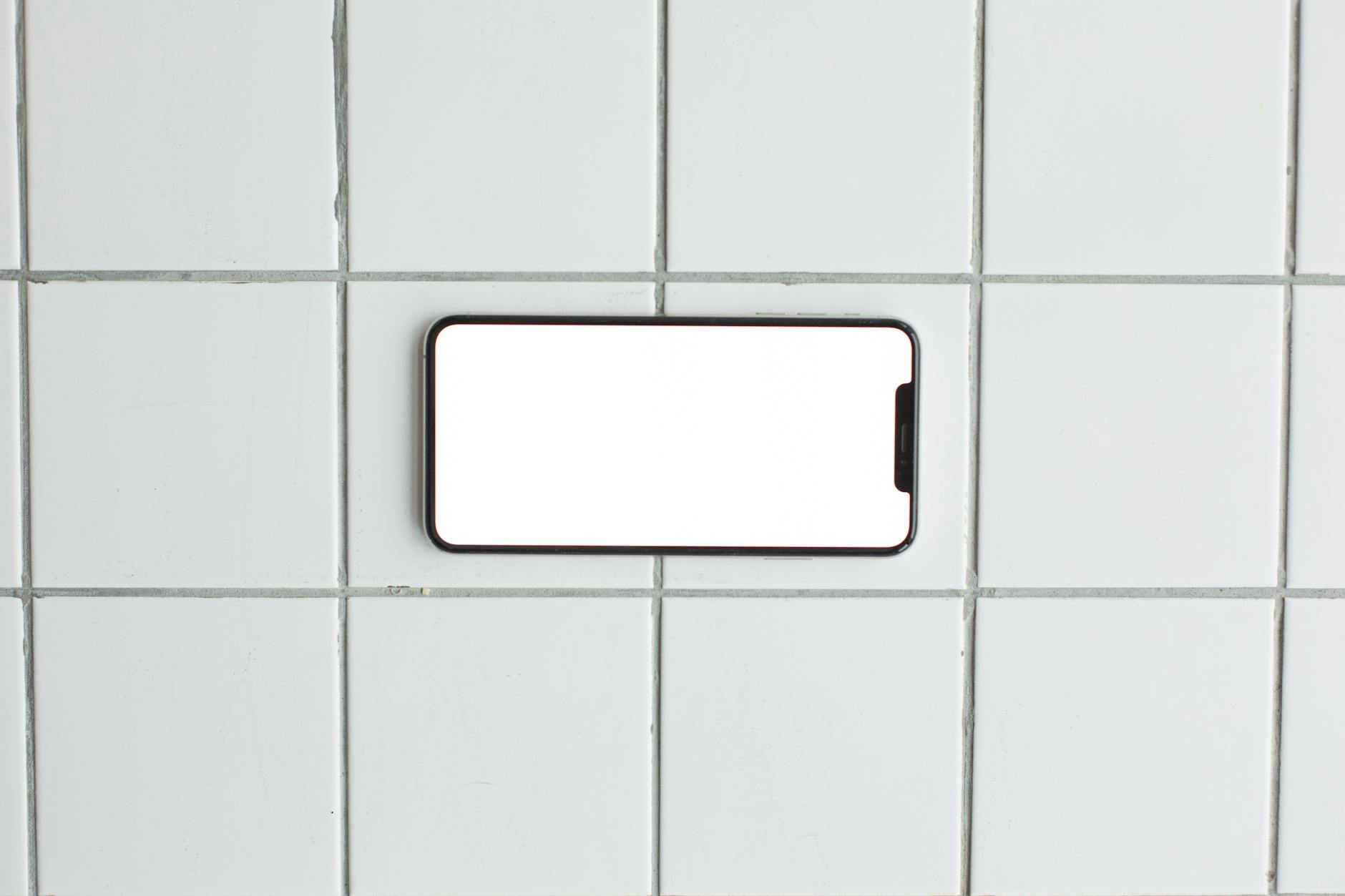 A blank smartphone mockup placed on a clean tiled surface, perfect for showcasing apps or designs.