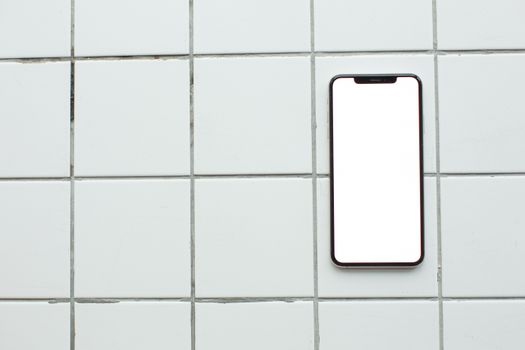 Top-down view of a smartphone with a blank screen on white tiles, ideal for mockup use.