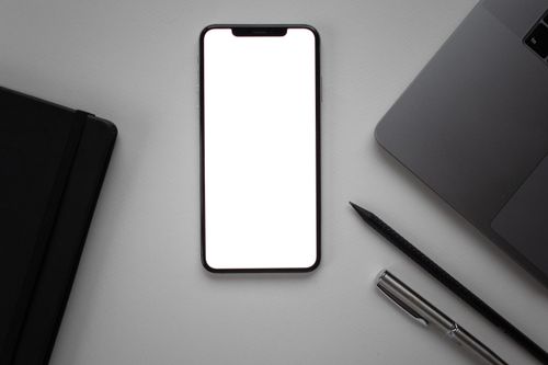 Free Flat lay of a sleek desk featuring a smartphone mockup beside a laptop, pen, and notebook. Stock Photo