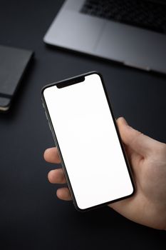 Close-up of a hand holding a smartphone with a white blank screen, ideal for mockup.