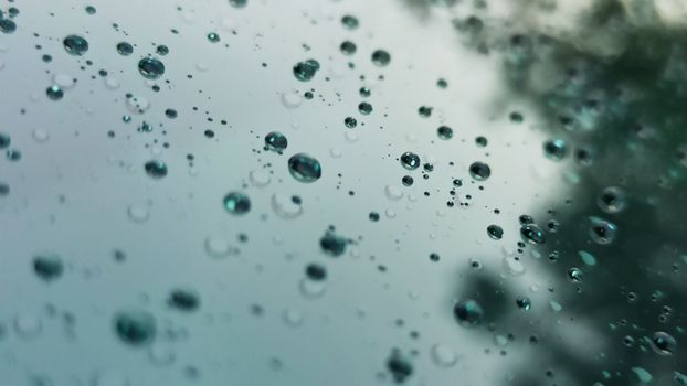 Detailed view of raindrops on a window with reflections on a cloudy day.