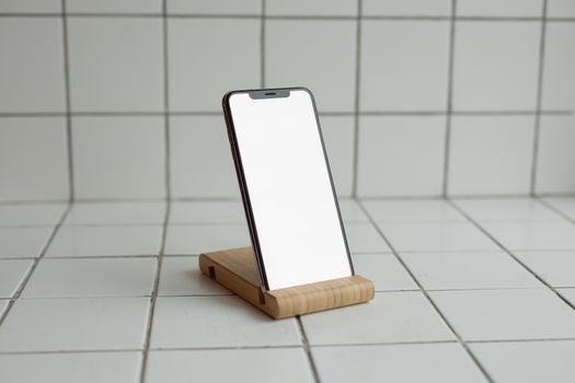 Modern smartphone on wooden stand with white ceramic tile background, minimalist design.