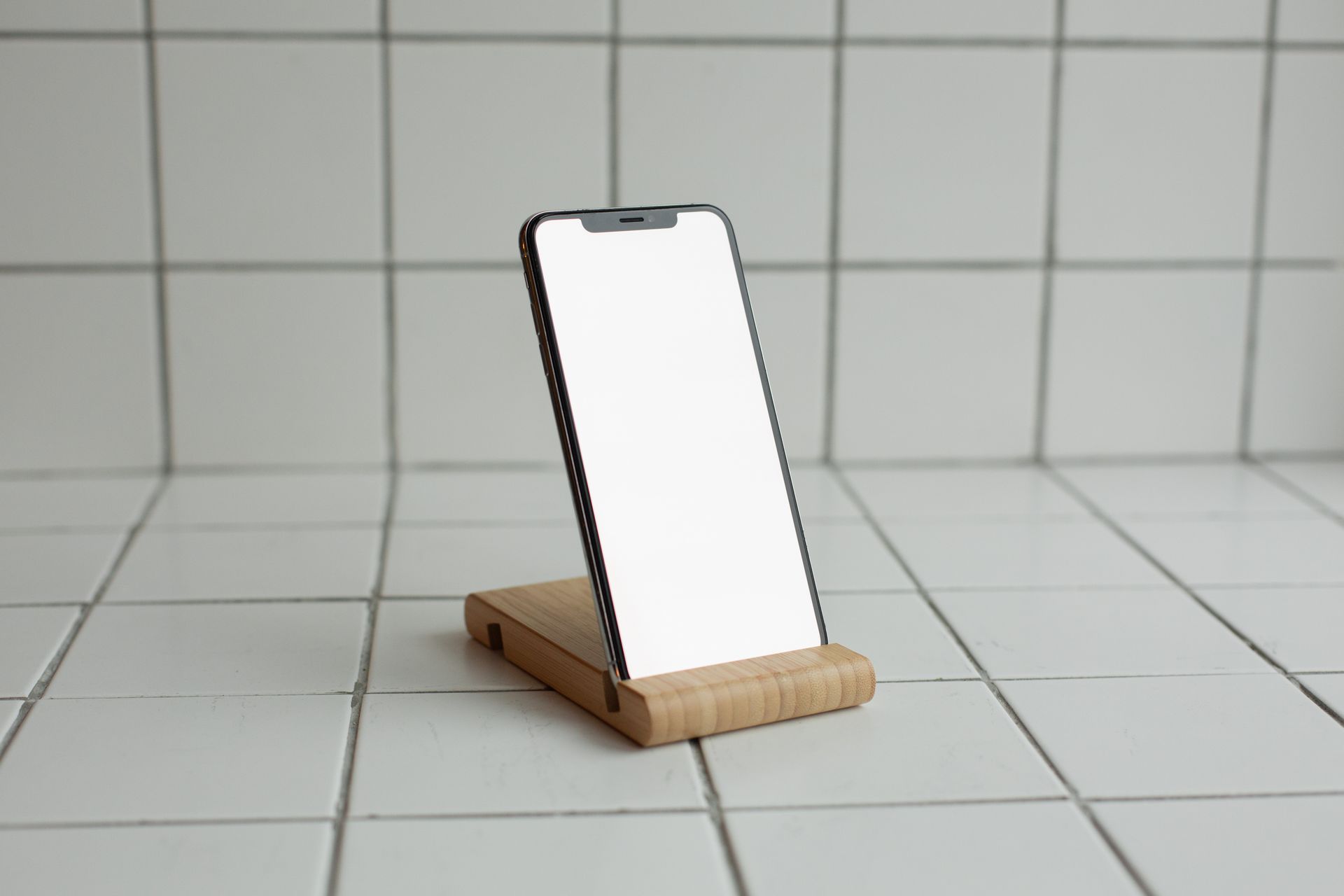 Modern smartphone on wooden stand with white ceramic tile background, minimalist design.