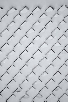 A chain link fence covered with snow, showing a geometric pattern typical of a winter scene in Estonia.