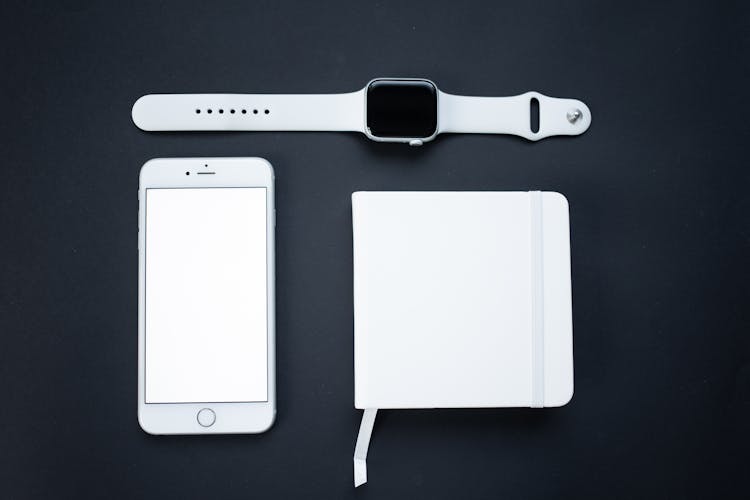 A Smartwatch Beside A Smartphone And A Notepad