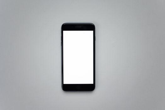 Top view of a black smartphone with a blank white screen on a gray surface.