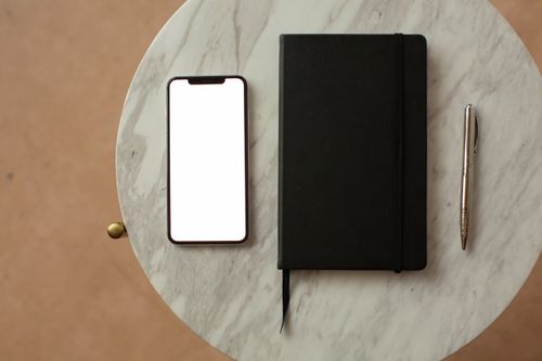 Free Flat lay of smartphone, notebook, and pen on a marble table, showcasing a sleek office setup. Stock Photo