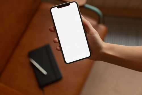 Free Close-up of a hand holding a blank smartphone screen indoors, perfect for mockup use. Stock Photo